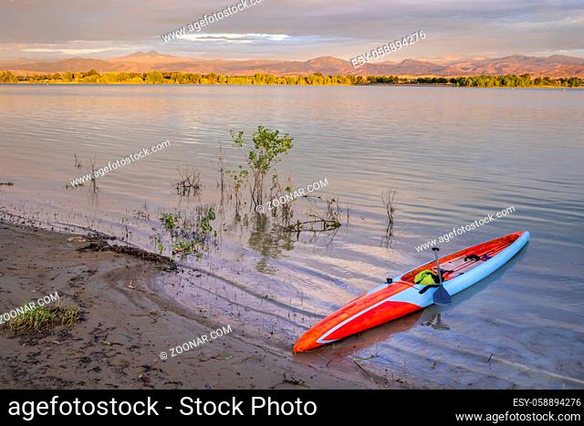 sunrise over Boyd Lake and Front Range of Rocky Mountains in northern Colorado with a long stand up paddleboard on a shore ready for paddling