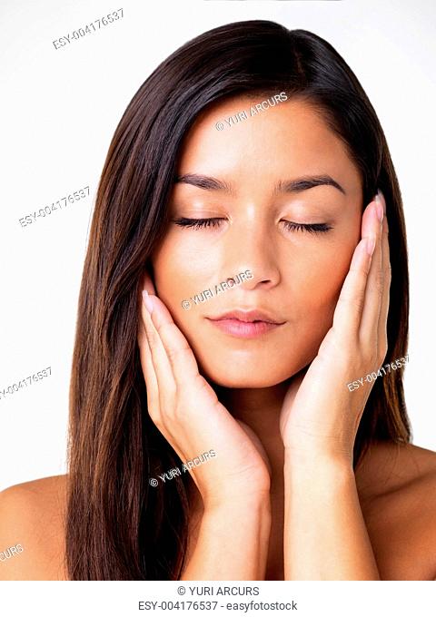 Closeup of a refreshed and glowing brunette with hands on her cheeks isolated on white