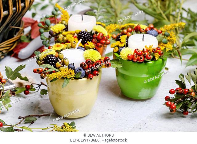 Candle holder decorated with autumn flowers and other plants. Making floral decorations at florist workshop