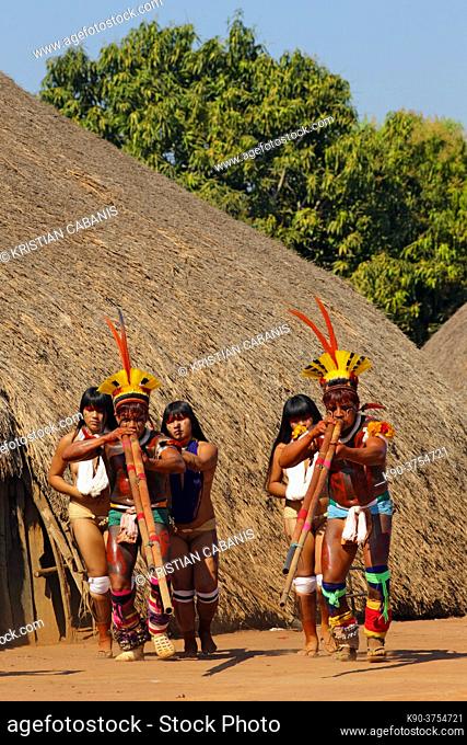 Two native indios withtwo young girls in festive clothing and feathres in their hair playing their long pipe, Mato Grosso, Brazil, South America