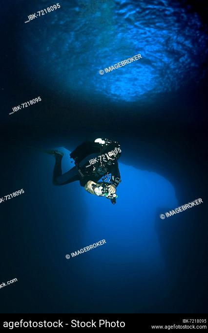 Diver dives with underwater lamp through rock grotto underwater cave Blue Dome with blue light in Blue Hole of Gozo, Mediterranean Sea, Gozo Island, Malta