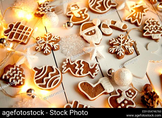 Christmas sweets composition. Gingerbread various shaped cookies with xmas decorations arranged on white wooden table with lights