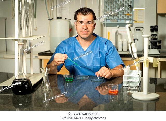 Middle age, Caucasian white, male laboratory technician in blue scrubs sampling with pipette chemical liquid solution in laboratory