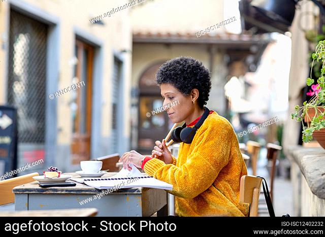 Italy, Tuscany, Pistoia, Woman sitting in outdoor cafe and looking through notes