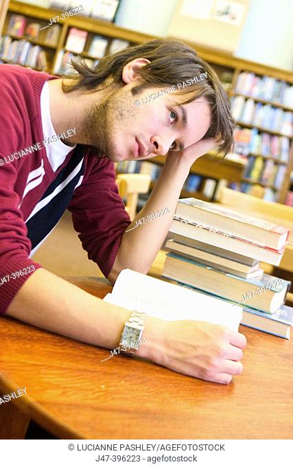 24 year old man leaning over a book, head in hand, in the library