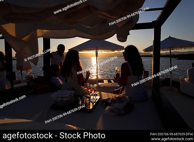 23 June 2020, Spain, Palma: Customers take a drink at sunset in the Bar Purobeach in Cala Estancia on the beach Playa de Palma