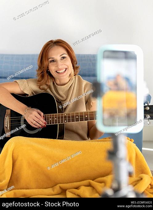 Influencer playing guitar filming through smart phone at home