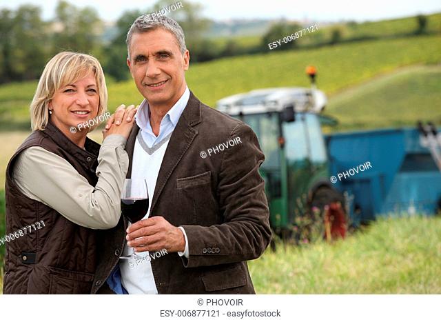 Farmer with glass of wine stood in front of tractor