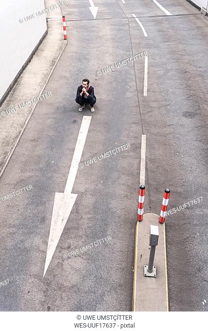 Businessman crouching on road with arrow sign