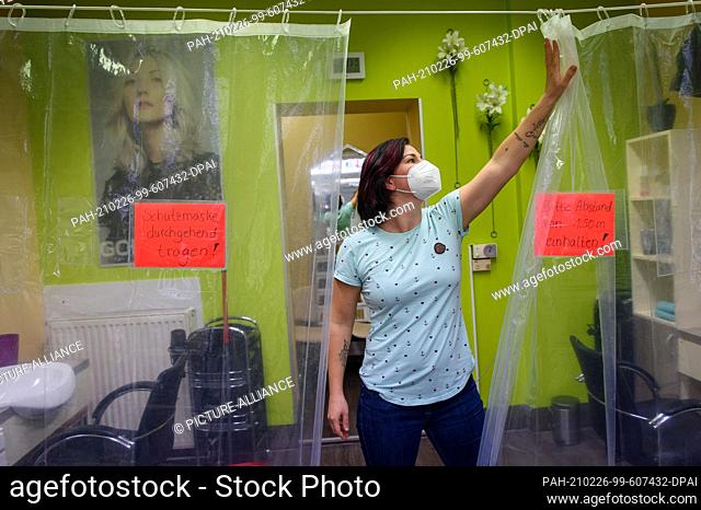 26 February 2021, Saxony-Anhalt, Magdeburg: Jacqueline Lucas, owner of ""Salon Stötzer"", pushes aside a protective curtain that stretches across the salon