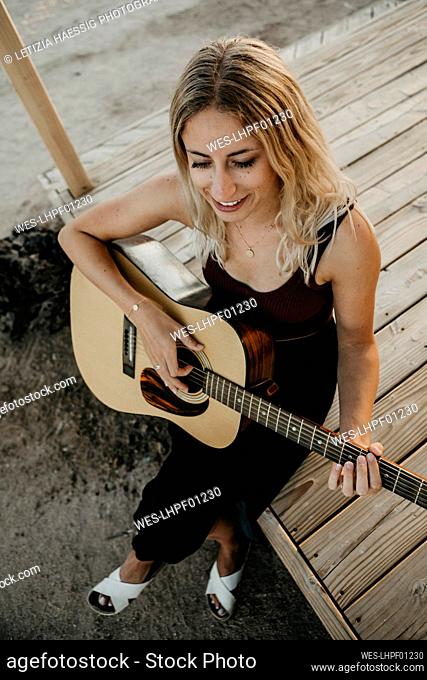 Smiling blond woman playing guitar outdoors, California, USA
