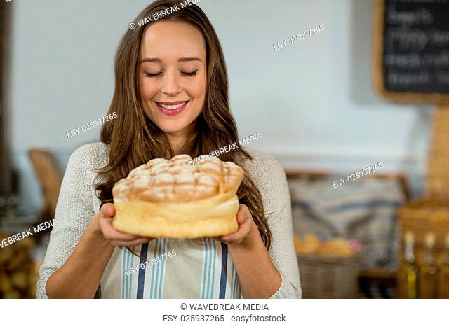 Smiling female staff holding round loaf of bread at counter