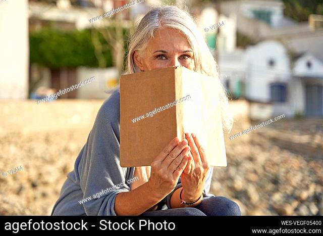 Woman covering face with book on sunny day