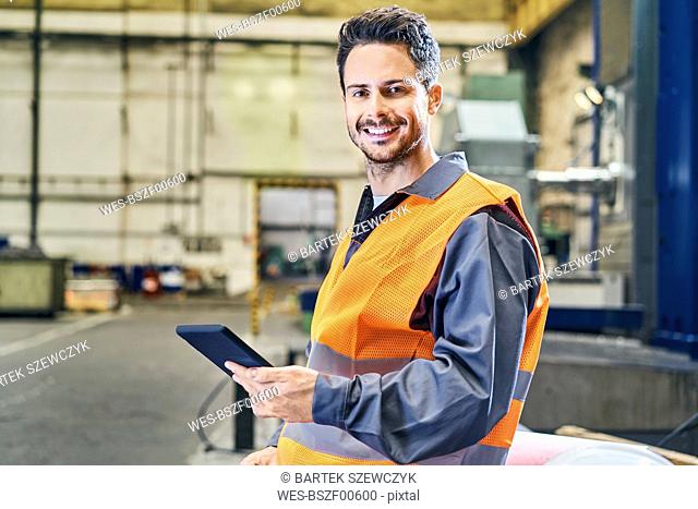 Portrait of smiling man holding tablet in factory