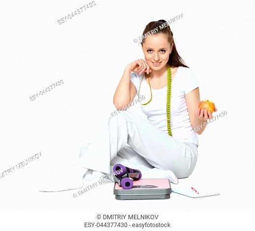 Young beautiful woman with scales, apple, dumbbells and notebook on a white background. Concept of healthy lifestyle