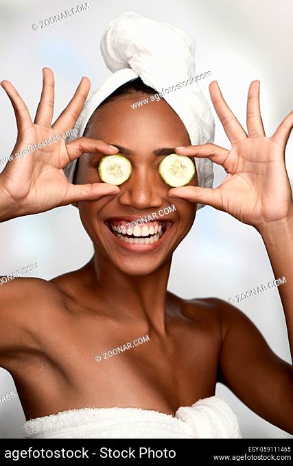Close-up portrait of a beautiful smiling woman with clean skin covering eyes with cucumbers isolated on white background