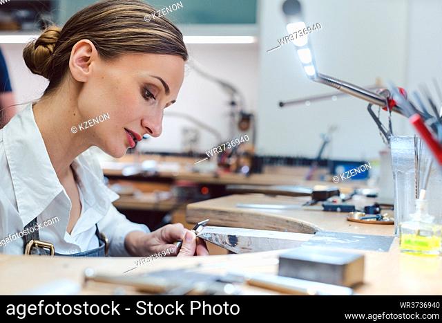 Jeweler working with tools on a piece of jewelry at her workbench