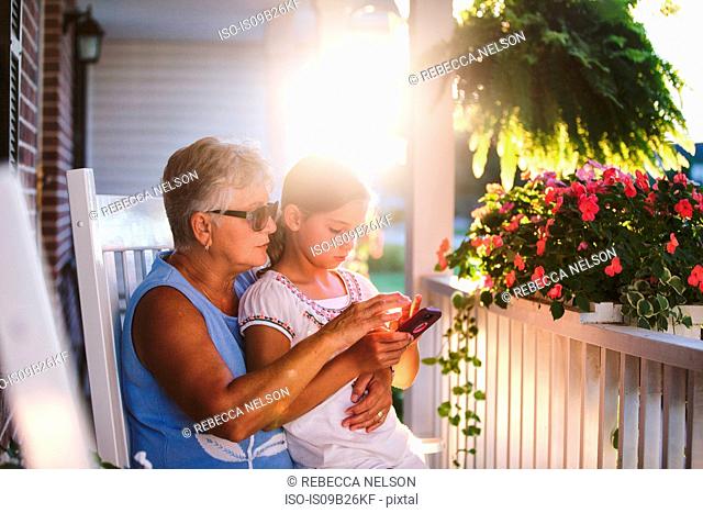 Girl and grandmother playing smartphone game on porch at sunset