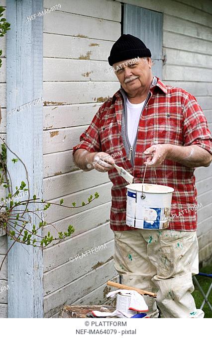 Elderly man painting his summer cottage Sweden