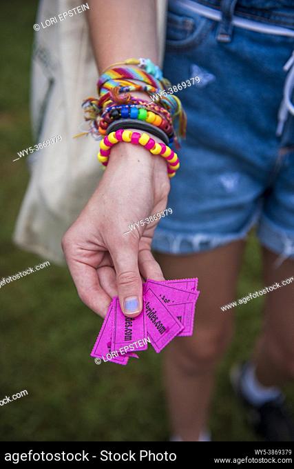A teenage girl wearing lots of colorful bracelets shows of her ride tickts at a county fair
