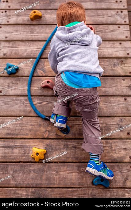 Sporty little boy climbing artificial boulder wall on an outdoor playground