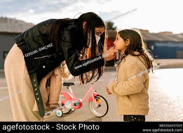 Mother wearing protective face mask cleaning face of daughter while standing on road