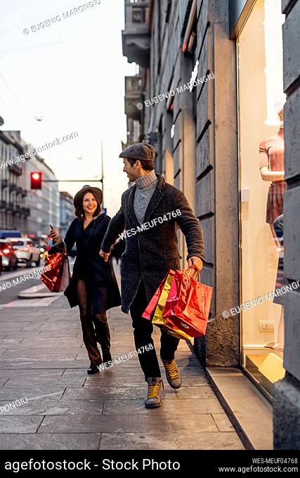 Cheerful young couple walking together with shopping bags in city