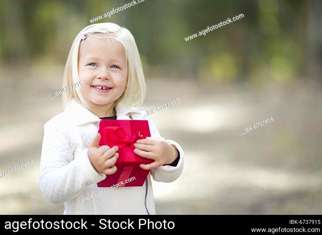 Happy baby girl holding red christmas gift outdoors