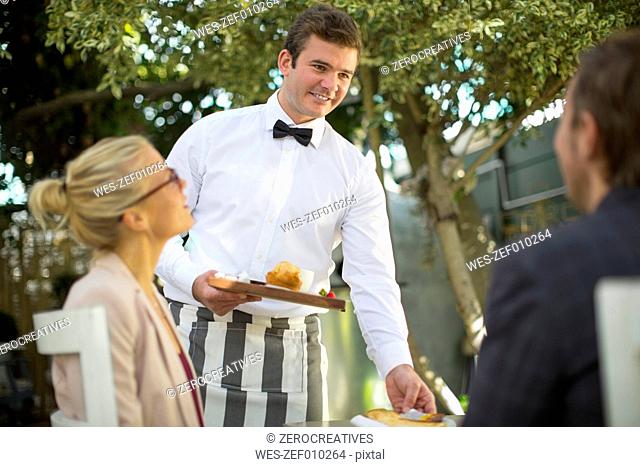 Waiter serving food at table for two