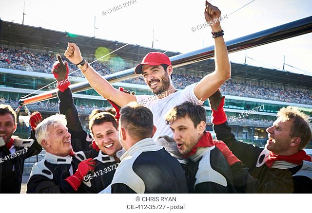 Formula one racing team carrying driver on shoulders, celebrating victory