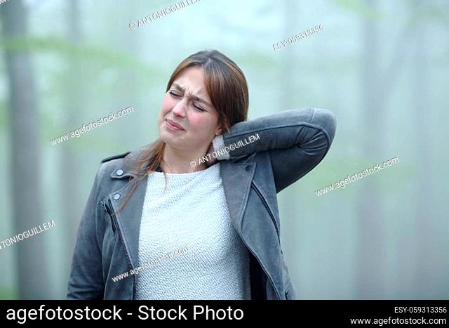 Woman suffering neck ache complaining alone in a foggy forest