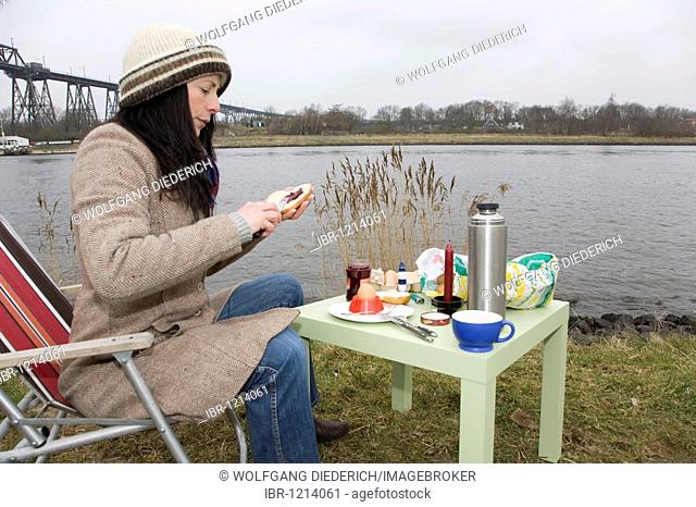 Young woman, 30-35 years, having breakfast on a damp winter day at the Kiel Canal, waiting for passing ships, Schleswig-Holstein, Germany, Europe