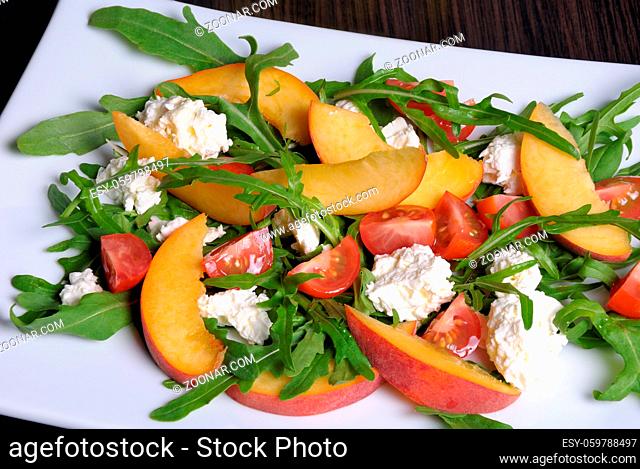 Salad with slices of peach, cherry tomatoes, arugula, feta
