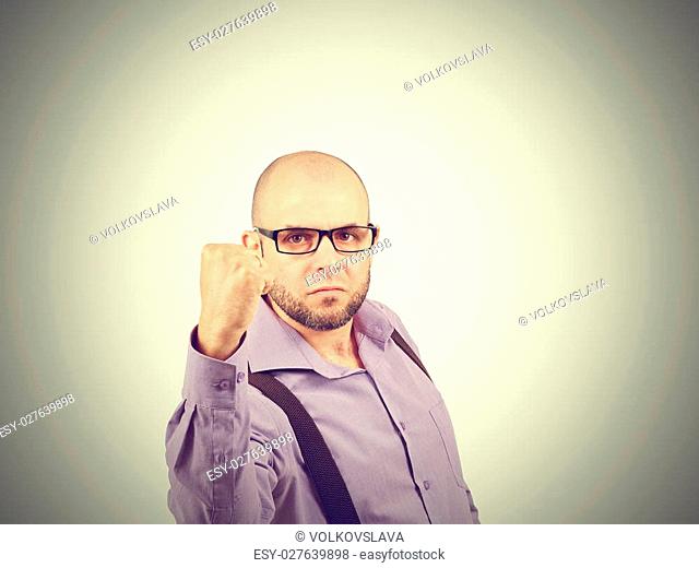 Angry businessman threaten with a fist . A bald man with a beard in a shirt with suspenders