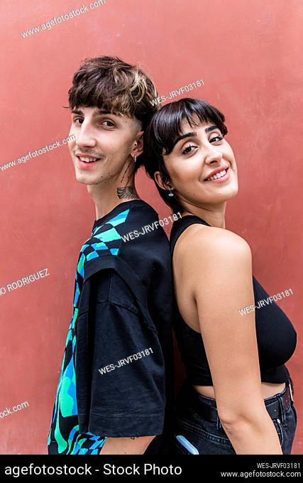 Smiling young couple standing back to back by red wall