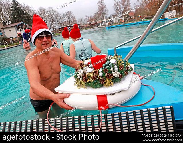 10 December 2023, Saxony-Anhalt, Osterwieck: Gerhard Schmuck from the Osterwieck ice sharks stands in the water with an Advent wreath at 6 degrees Celsius in...