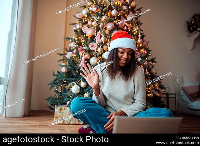 Female wearing santa smiling while speaking with online friend on laptop during Christmas celebration at home