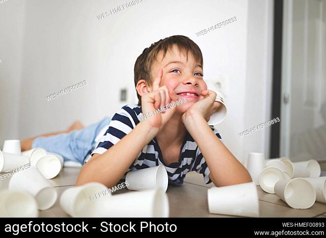 Portrait of smiling little boy lying on the floor between white paper cups