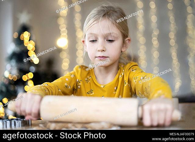 Blond girl rolling out dough on table at home