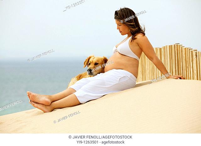 Pregnant woman relaxing on the beach with her dog