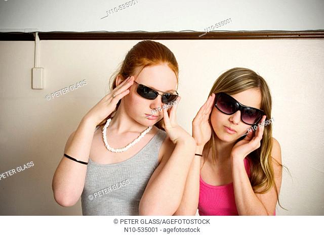 Long red-hair and blond-hair teen girls, both wearing sunglasses, clowning around together