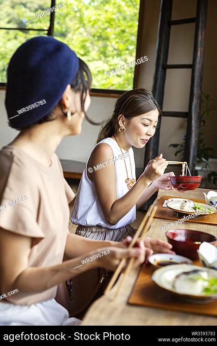 Two Japanese women sitting at a table in a Japanese restaurant, eating