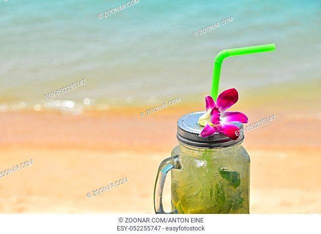 Big jars mug style full glass of fresh frozen mojito with metal cap lid, straw and purple orchid flower in cafe on the beach