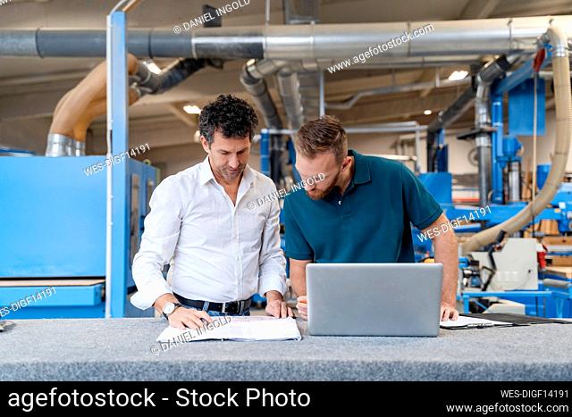 Two carpenters talking over documents in production hall