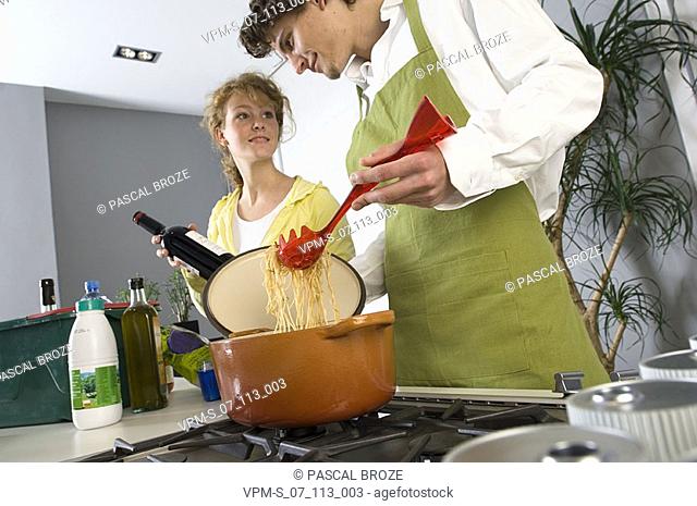 Side profile of a young man cooking noodles with a young woman smiling beside him