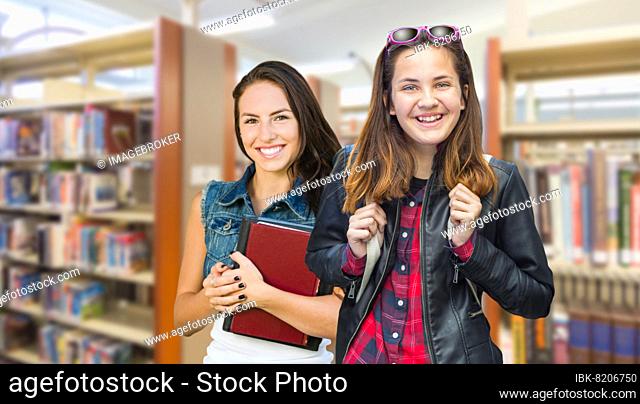mixed-race female students wearing backpack and books walking in the library
