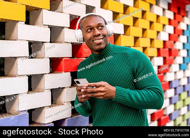 Smiling man holding mobile phone by multi colored wall