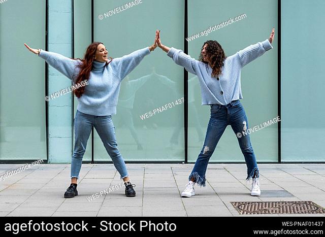 Friends wearing blue sweater giving high-five while standing on footpath
