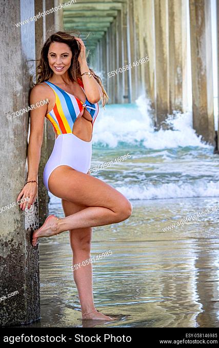 A beautiful brunette bikini model poses under the pier