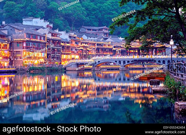 Chinese tourist attraction destination - Feng Huang Ancient Town (Phoenix Ancient Town) on Tuo Jiang River with bridge illuminated at night